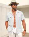 Detailed view of men's casual short-sleeve linen shirt with chest pockets worn by model outdoors. - White