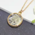 Close-up detail of a round gold necklace pendant featuring real white dried flowers inside glass - White Snow Flower Round Gold Necklace