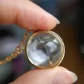 Close-up of a clear glass ball pendant with real dandelion seed inside on gold chain - Dandelion Spherical Gold Necklace
