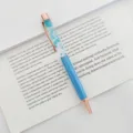 Elegant blue dried flower ballpoint pen with rose gold accents on a book page - 1.0mm Bullet Tip / Blue
