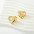 Vista detallada de pendientes de corazón huecos dorados sobre soporte ondulado blanco. - Estilo de corazón orgánico irregular (Fig 5)