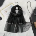 Vue de détail d'un foulard transparent en organza noir avec rayures dorées et perles. - Noir