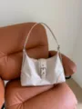 Detailed view of an elegant cream hobo underarm bag with buckle on a brown leather armchair - 33*9.5*21cm / White