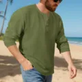 Close-up shot of men's textured green long-sleeve Henley shirt with button placket on beach. - Army Green