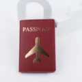 Dettaglio ravvicinato del porta passaporto in pelle PU rossa con aereo e testo dorati. - Borgogna
