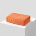 Oranje effen katoenen badhanddoek, netjes gevouwen op standaard, zachte badstof textuur. - 140x70cm / Koraaloranje