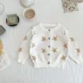 Detailed view of the cozy white knitted baby cardigan featuring gold star patterns and front buttons. - 66cm / White