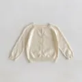 Vue détaillée d'un gilet tricoté pour bébé crème avec de jolies boules et boutons. - Abricot Beige / 66cm