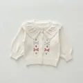 Detailed view of white baby knitted cardigan featuring delicate floral embroidery and ruffle collar. - 66cm / White & Apricot Jacket
