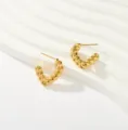 Vista detallada de pendientes de aro retorcidos chapados en oro de 18K con textura pulida. - Estilo de Giro Trenzado