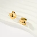 Primer plano de pendientes de aro dorados gruesos minimalistas en soporte expositor ondulado. - Estilo de Cara Ancha Tridimensional de Pared Gruesa