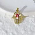 Primo piano di un ciondolo a mano di Fatima dorato con motivo malocchio e zirconi lucenti. - Stile Mano Di Fatima In Smalto Bianco (xz422-4) / Oro