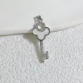 Close-up of a gold-plated key pendant featuring mother-of-pearl clover and zircons. - White