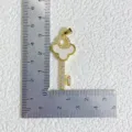 Detail view of gold-plated key pendant with mother-of-pearl and zirconia size reference. - Gold