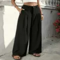 Outdoor detail shot of high-waisted black pleated wide-leg trousers showcasing drape and pocket. - Black