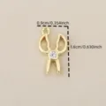 Dettaglio del ciondolo a forbice dorata con dimensioni di 1,6 cm e zircone brillante. - Oro