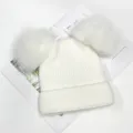 Close-up detail of white double pom-pom knit beanie, fluffy fur balls and warm fleece lining. - White