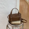 Borsa a tracolla cilindrica vintage marrone con doppi manici e fibbie decorative. - Marrone