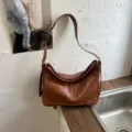 Detail view of vintage brown leather shoulder bag, highlighting the front pocket and strap. - With Pendant / Tan