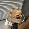 Primo piano di un mini zaino beige con trapuntatura, manico a fiocco e grazioso orsetto di peluche. - Con Ciondolo / Bianco avorio
