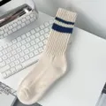 Detail view of cream crew socks with navy blue varsity stripes on a white desk - Dark Blue Double Stripes (Beige Body)