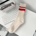 Close-up of cream athletic crew socks with dual red stripes on a white desk. - Red Double Stripes (Beige Body)