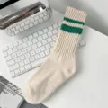 Detailed view of beige varsity-style crew socks with green stripes on a white desk - Green Double Stripes (Beige Body)