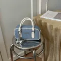 Close-up detail of stylish quilted denim shoulder handbag with white trim and chic metal charm. - With Pendant / White with Pendant