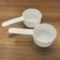 Weiße Kunststoff-Messlöffel für Milchpulver oder Backen auf einer Holzoberfläche - 15g 30ml Weiß ohne Skala