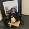 Primer plano detallado del elegante bolso saco negro con un lindo dije de osito de peluche. - Con Colgante / Negro