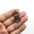Nahaufnahme eines schwarzen Metallspinnen-Anhängers mit rotem Kristallkörper für Halloween DIY-Schmuck. - Schwarze Spinne Roter Strass