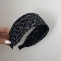 Vista dettagliata di un cerchietto nero largo con motivo floreale bianco fine e tessuto. - Foglia / Nero