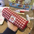 Close-up detail of red and white plaid pencil case showing cute character embroidery patch. - Red Plaid Apple Cylindrical Pencil Case