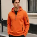 Detailansicht des orangefarbenen Kapuzensweatshirts mit halbem Reißverschluss und Taschen. - Orange