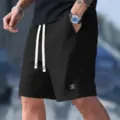 Detail view of black waffle knit men's casual shorts with white drawstrings and logo patch. - S / Black
