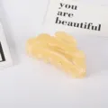 Detalle de una pinza para el pelo de acetato amarillo crema sobre un fondo blanco minimalista - Rosa loto