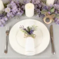 Vista dettagliata di un portatovagliolo con fiore viola artificiale e fiocco di iuta rustico. - Bianco