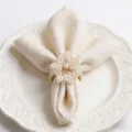 Elegant gold pearl napkin ring table decor set with cream napkin on white ceramic plate. - Off White