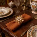 Dettaglio di un portatovagliolo a fiore dorato con perle e strass su tessuto elegante. - Oro