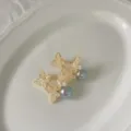 Detail van gouden vlinder parel oorbellen met sprankelende zirkonia op witte schaal. - Goud Grijze Parel