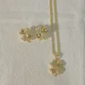 Gedetailleerde close-up opname van de klaverbladhanger ketting en de bijpassende oorbellen. - Goud Klaver Stijl