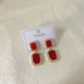 Primo piano degli orecchini geometrici in cristallo rosso con bordo dorato pavé. - Quadrato Rosso