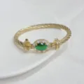 Squisito dettaglio del bracciale rigido dorato intrecciato con una bella pietra verde. - Oro e Verde