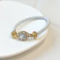 Primo piano del bracciale in pelle intrecciata bianca con zircone ovale placcato oro. - Bianco