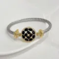 Detailed view of copper 18k gold plated cable cuff bracelet with black zircon flower charm. - Black