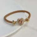 Primo piano del bracciale in pelle marrone con zircone cuore rosa e dettagli dorati. - Cammello