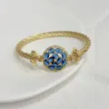 Detailed close-up of a gold-plated cable twist bangle with a sparkling blue zircon floral center. - G Blue