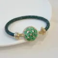 Close-up detail of the 18k gold plated green zircon flower clasp and braided leather band. - Green
