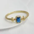 Bracciale rigido dorato a treccia con pietra blu rettangolare e zirconi luminosi. - Oro e Blu