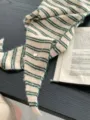 Knit stripe triangular scarf detail shot showing cozy texture and green pattern on beige. - Army Green